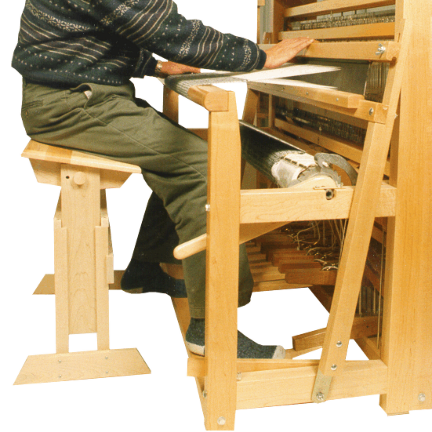 Weaver seated on the Leclerc Rocking Bench at a floor loom, demonstrating ergonomic posture and adjustable seat height for improved treadling and long weaving sessions.