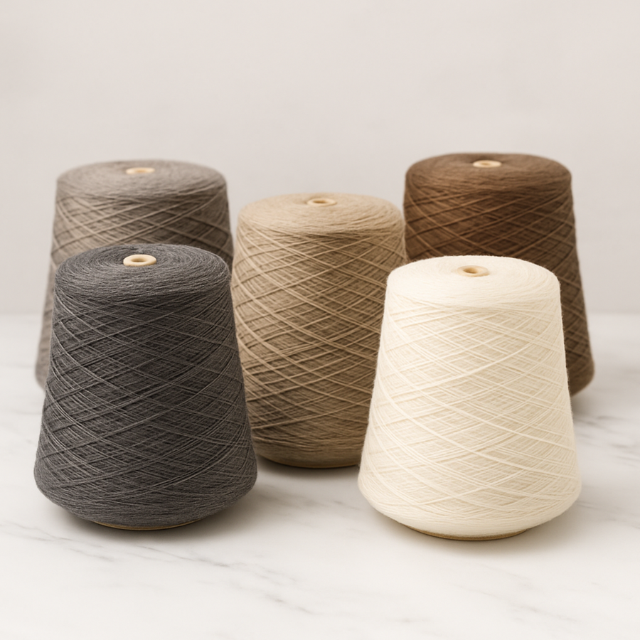 5 cones of Brown Sheep Nature Spun Sport Yarn in Neutral color tones against a white marble backdrop.