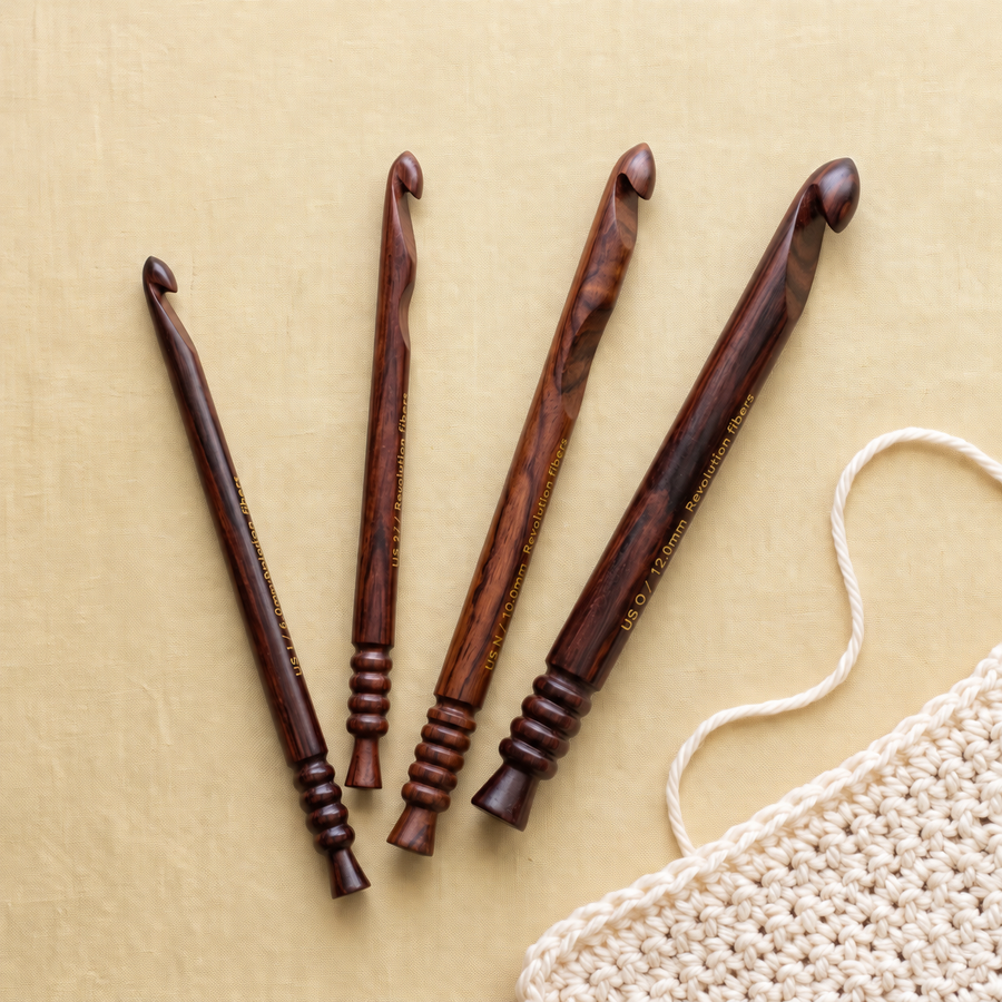 Four rosewood crochet hooks arranged on pale gold fabric beside an ivory crochet swatch.