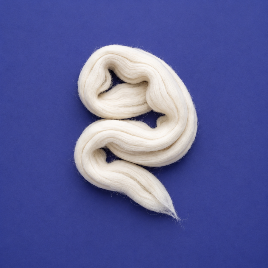 Natural ivory Merino combed wool top arranged in loose folds on an indigo background.