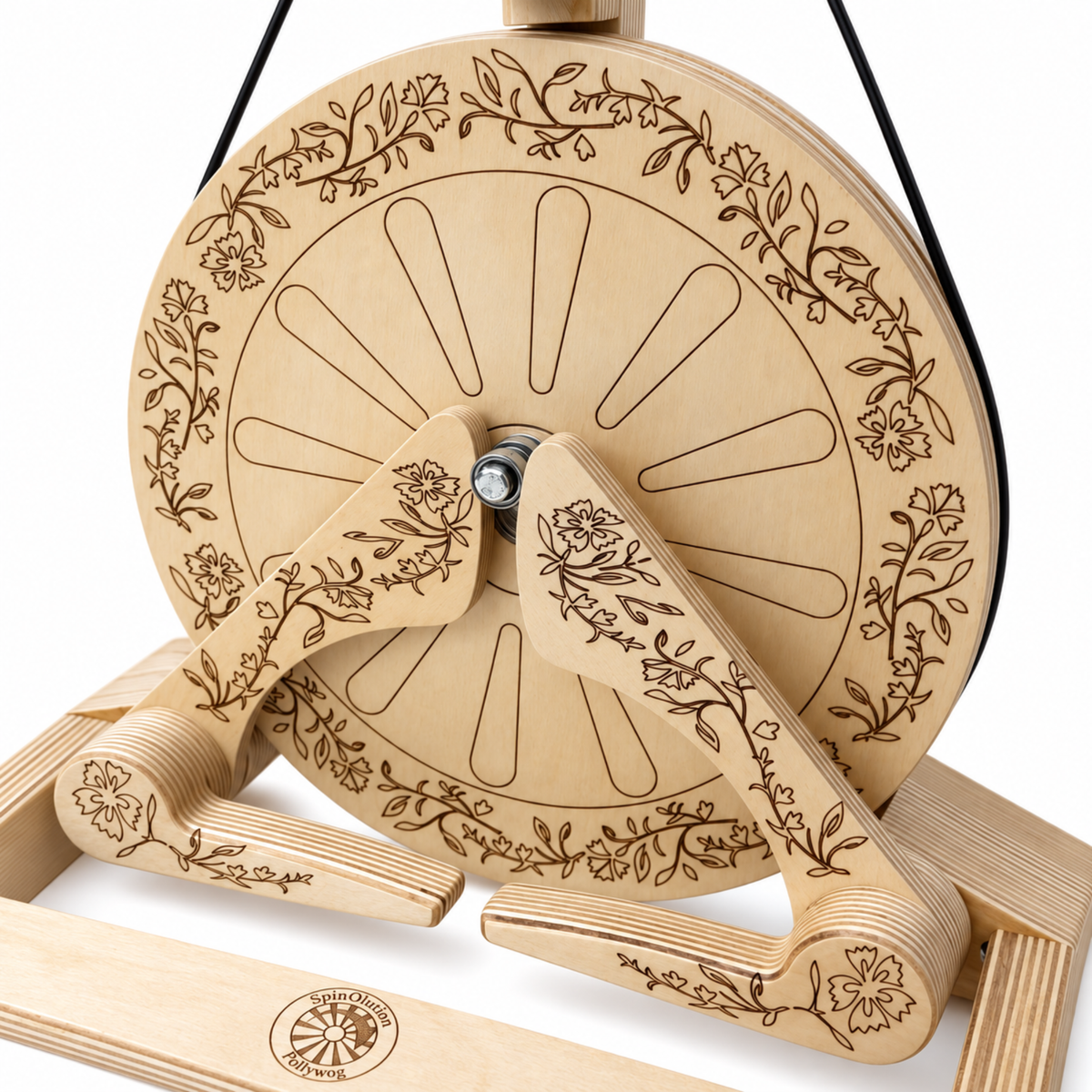 Close-up of the SpinOlution Pollywog spinning wheel showing intricate floral engraving on the wooden drive wheel, treadles, and frame.