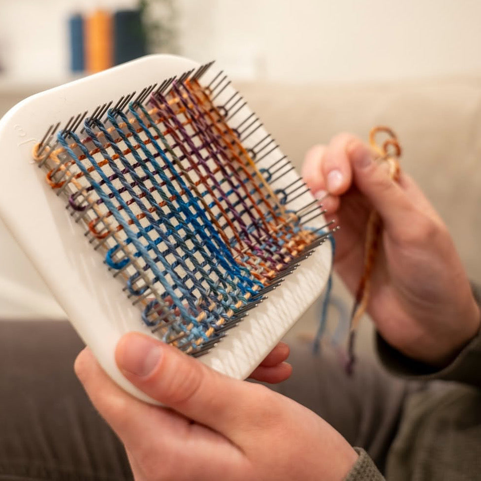 Schacht Zoom Loom with an orange woven fabric in progress on the 4x4 pin loom. Perfect for small, portable weaving projects and beginner-friendly fiber arts.