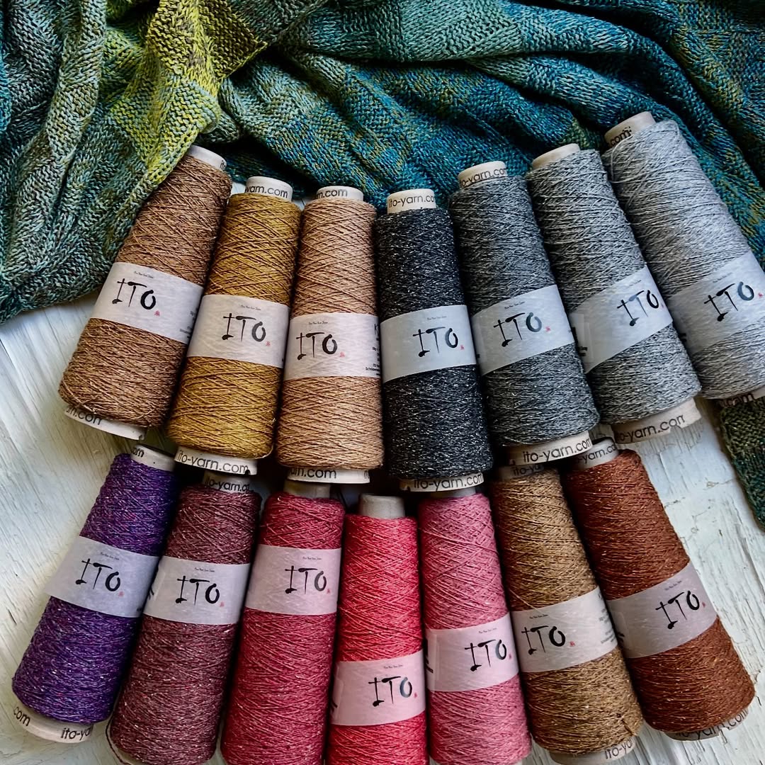 Complete collection of Ito Yarns Kinu Organic Silk Noil Weaving Yarn cones in all available colors: Black, Dark Navy, Navy Blue, Sugar Plum, Angora, Salvia Blue, Iron Blue, String, Camel, White, Light Gray, Pool Green, Violet, and Cherry Blossom. Made from organic silk noil and recycled fibers, these yarns feature a rustic texture, matte finish, and a melange of blended hues perfect for weaving, knitting, and crocheting projects.