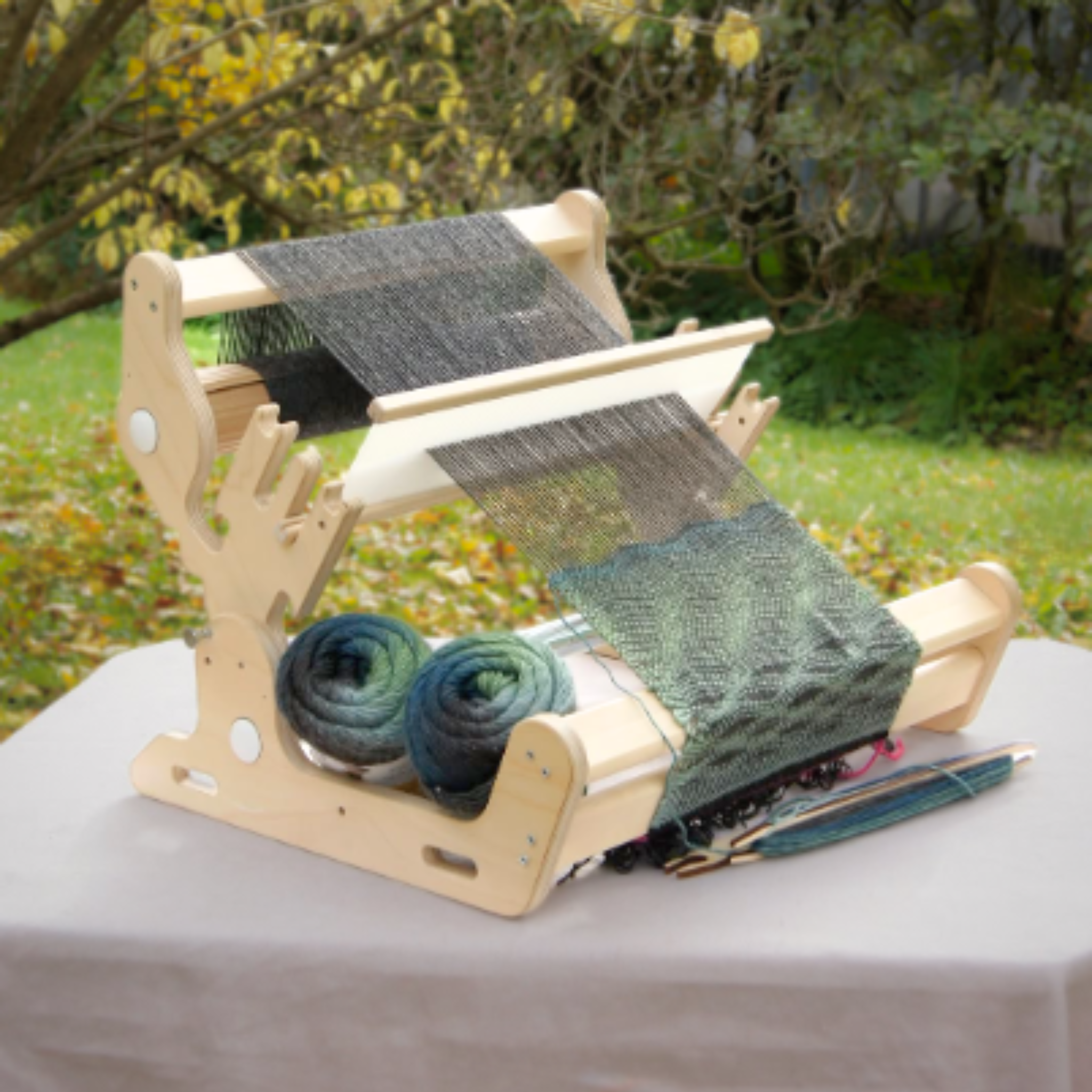 Glimakra Siru Rigid Heddle Loom set up outdoors with a weaving project in progress. Featuring an ergonomic design, adjustable warp beam, and sturdy construction, this loom is ideal for portable weaving and supports both beginner and advanced textile artists.