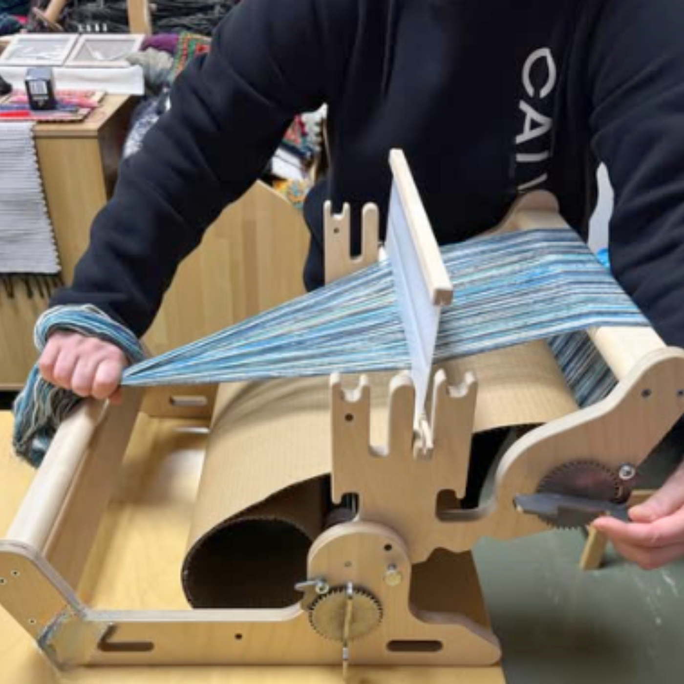 Weaver using the Glimakra Siru Rigid Heddle Loom, demonstrating its ergonomic design and smooth weaving process. The adjustable angle and sturdy stainless steel ratchet system provide excellent tension control for effortless and precise weaving.