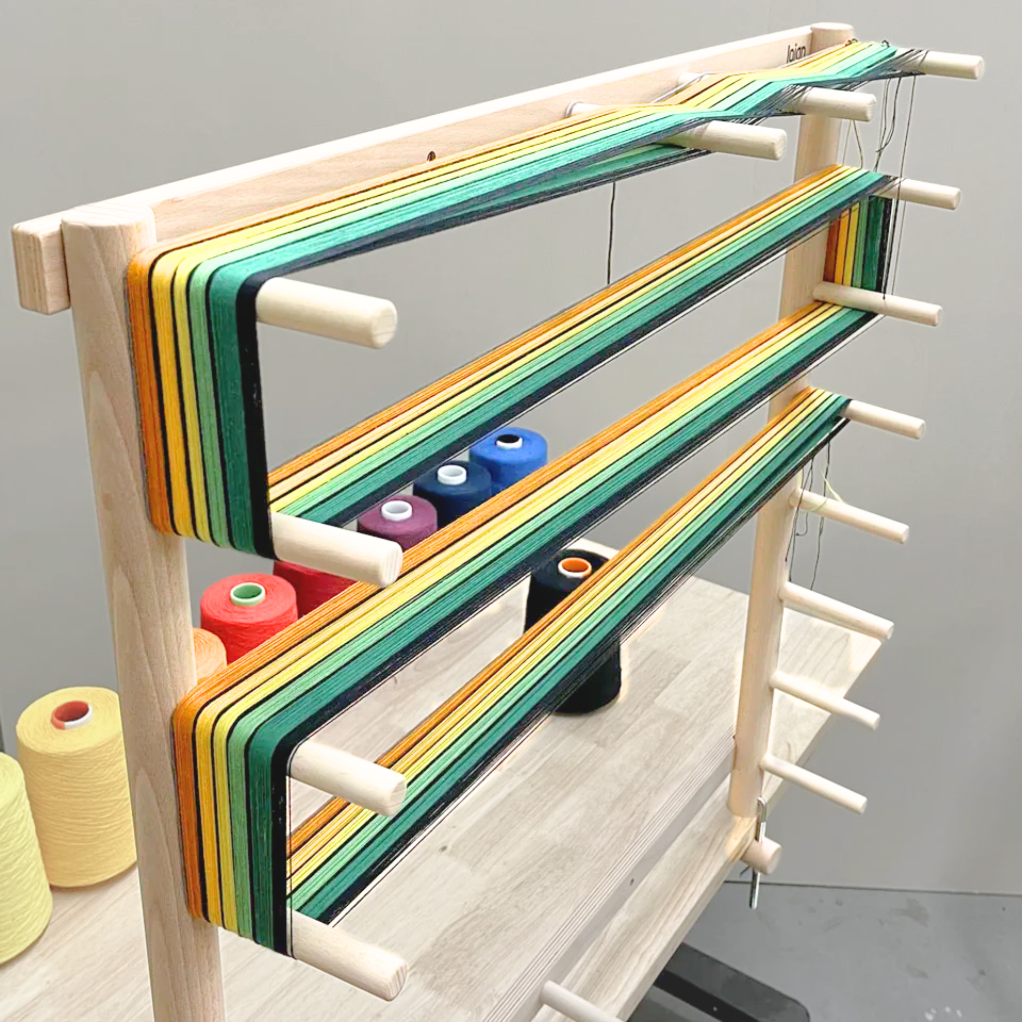 Lojan Warping Frame in use with green, yellow, and black warp threads wrapped around pegs.