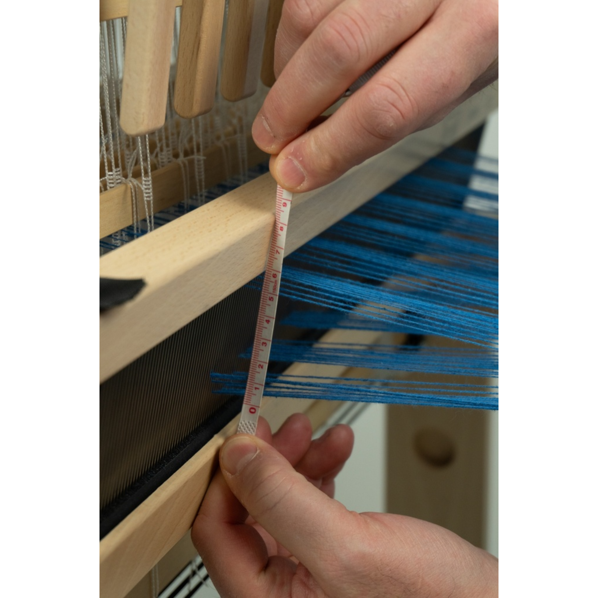 Close‑up of hands measuring the shed on a Louët Jane 16‑shaft table loom, showing easy warp insertion.
