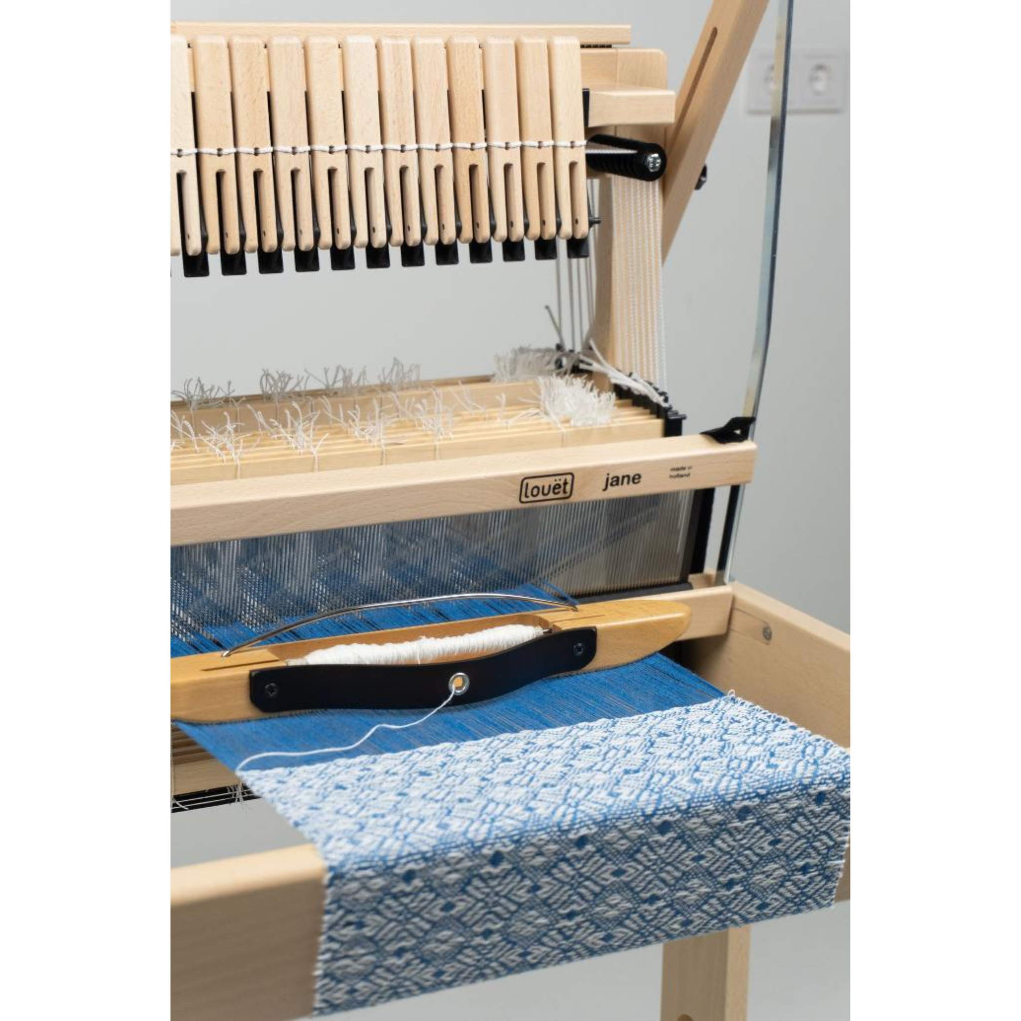 Weaving area of the Louët Jane loom with blue fabric in progress and shuttle resting on the beater shelf.