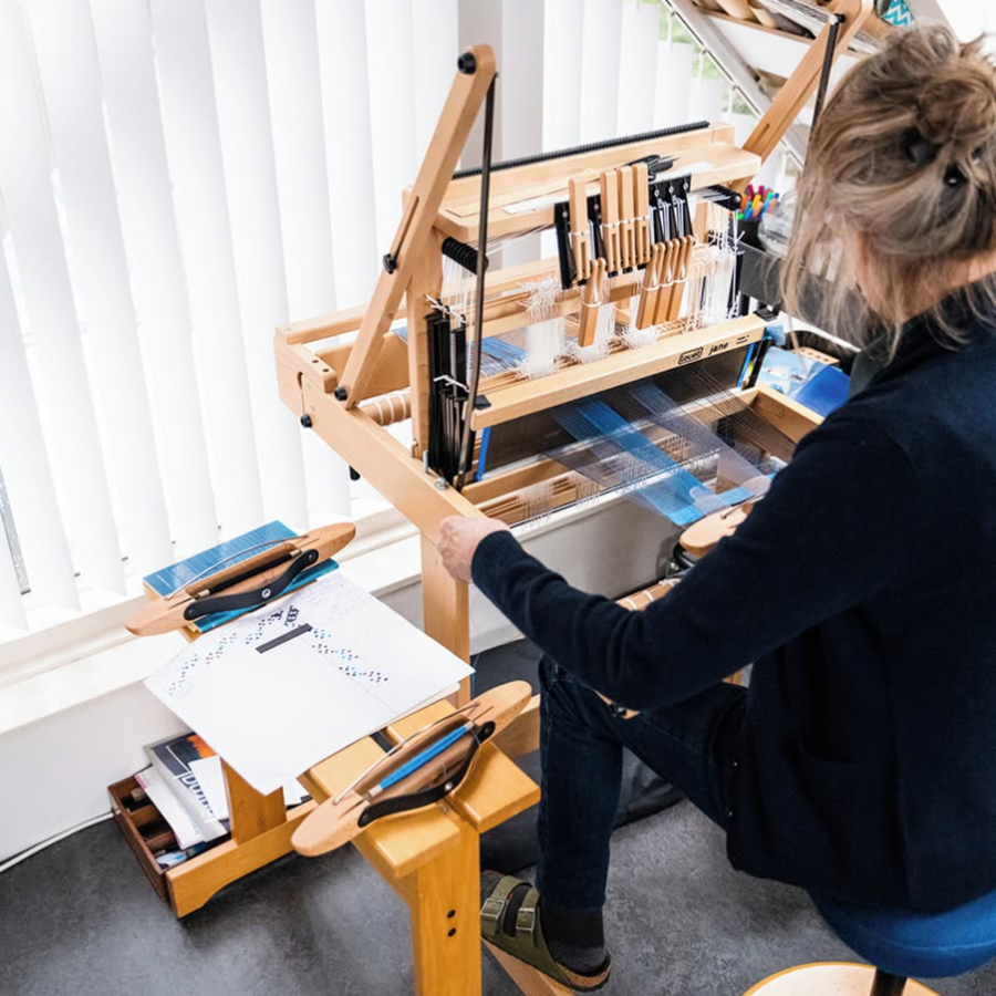 A weaver weaving on the Louët Jane 8-shaft table/floor loom in her studio.
