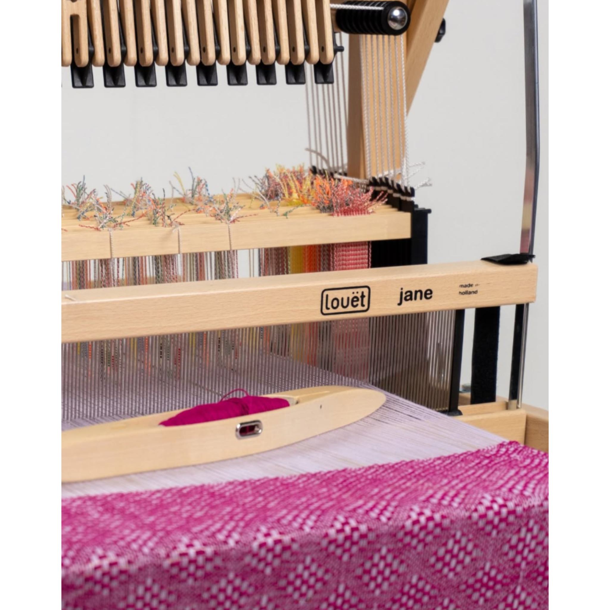 Front angle of the Louët Jane loom demonstrating wide shed and pink sample cloth on the cloth beam.