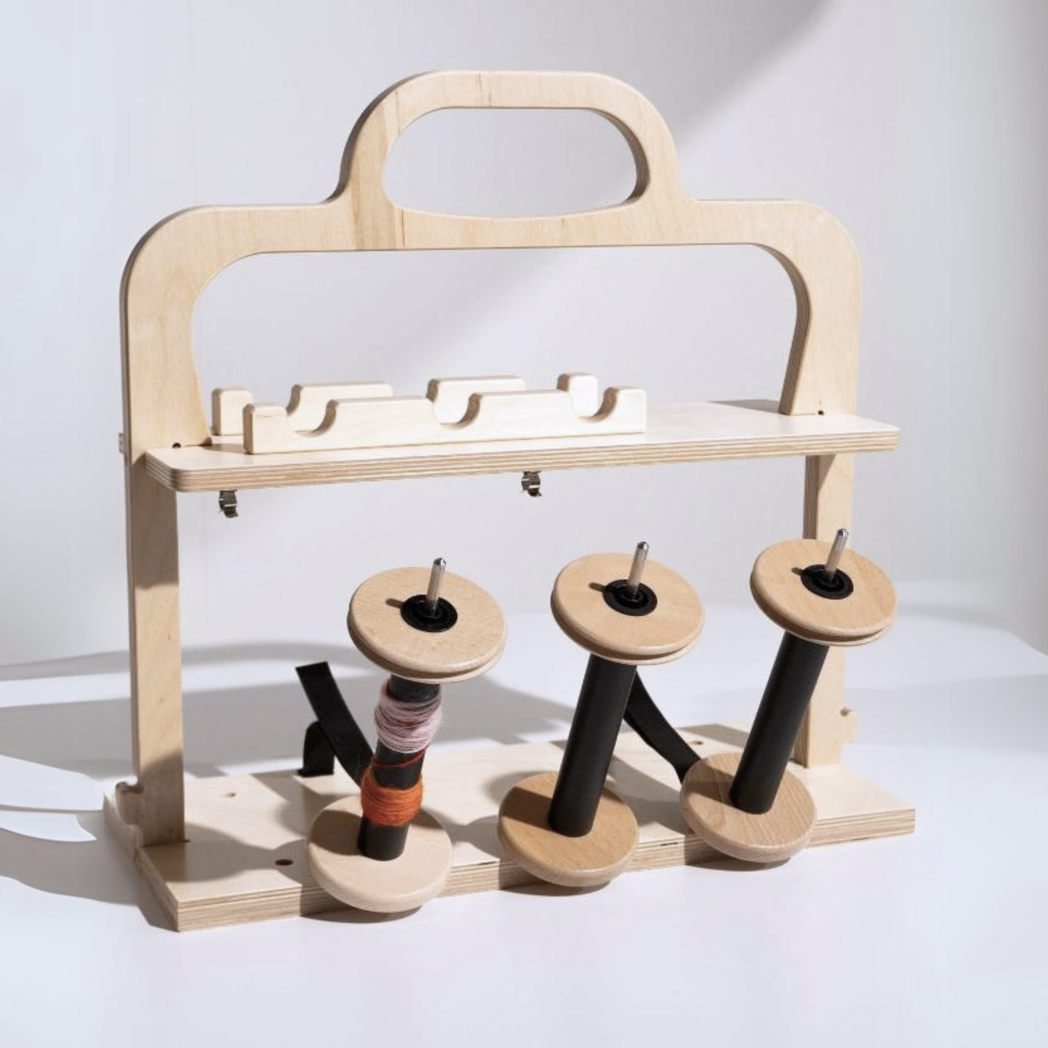 Louet Jenn-E Electric Spinning Wheel wooden lazy kate with three bobbins, showcasing a convenient setup for plying and organized yarn management.