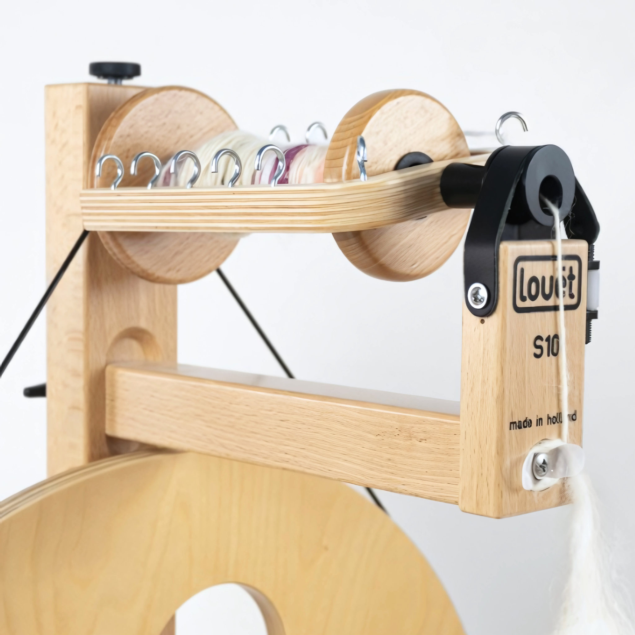 Close-up view of the Louet S10 spinning wheel flyer and adjustable hooks, showing yarn winding on the bobbin and durable beechwood construction.