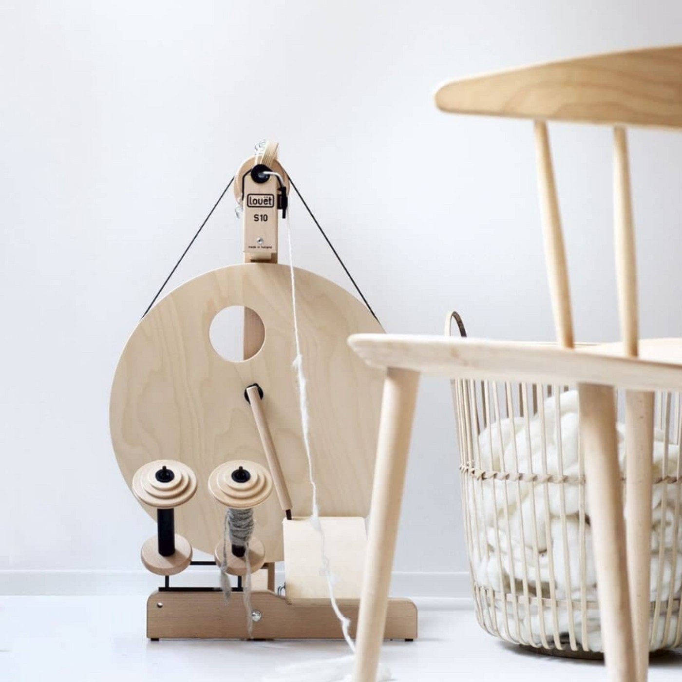 Louet S10 Irish Tension Spinning Wheel in a modern studio setting with chair and fiber basket, ideal for home spinners and fiber artists.