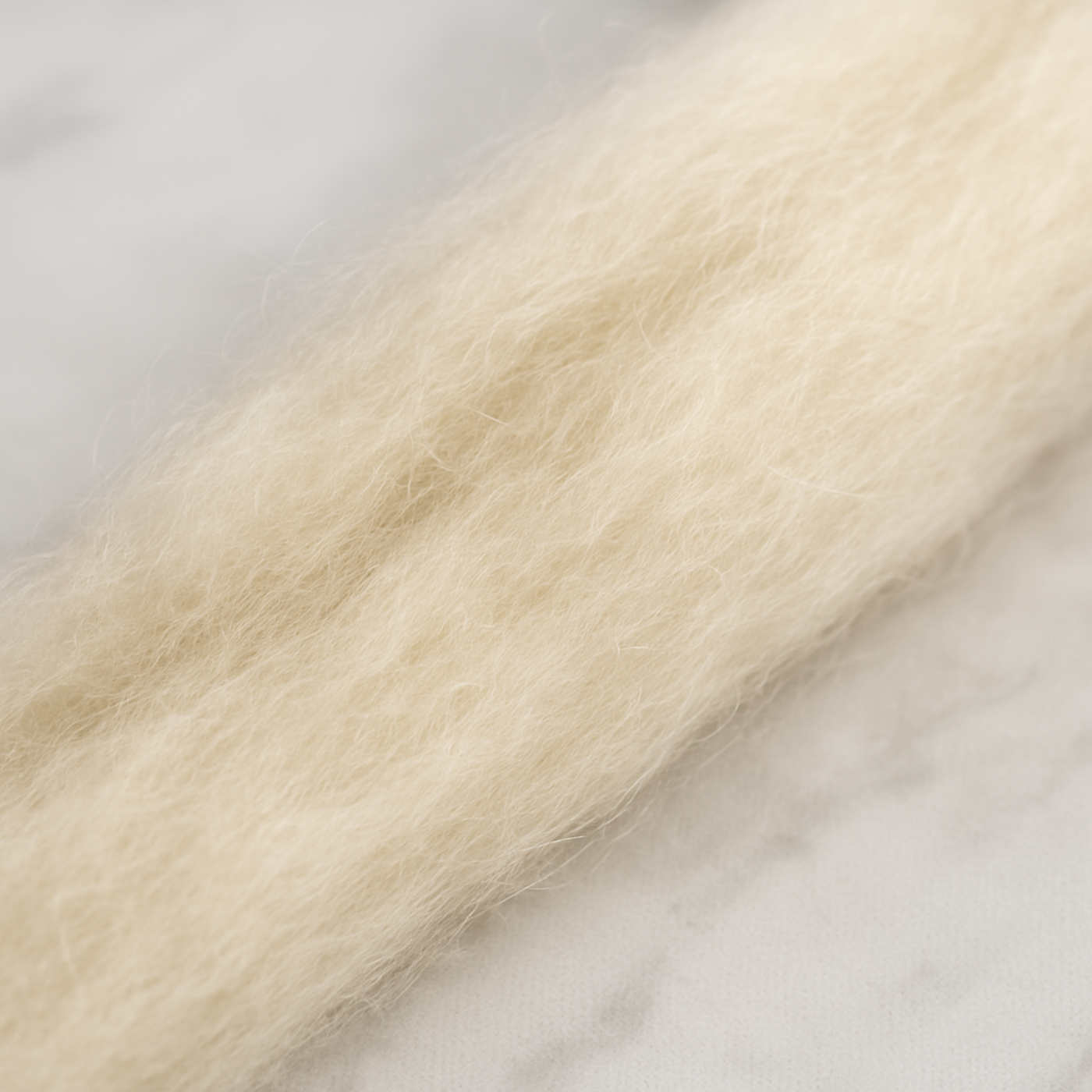 Close-up texture of 19 micron undyed Merino wool carded sliver on white marble, showing airy matte loft.