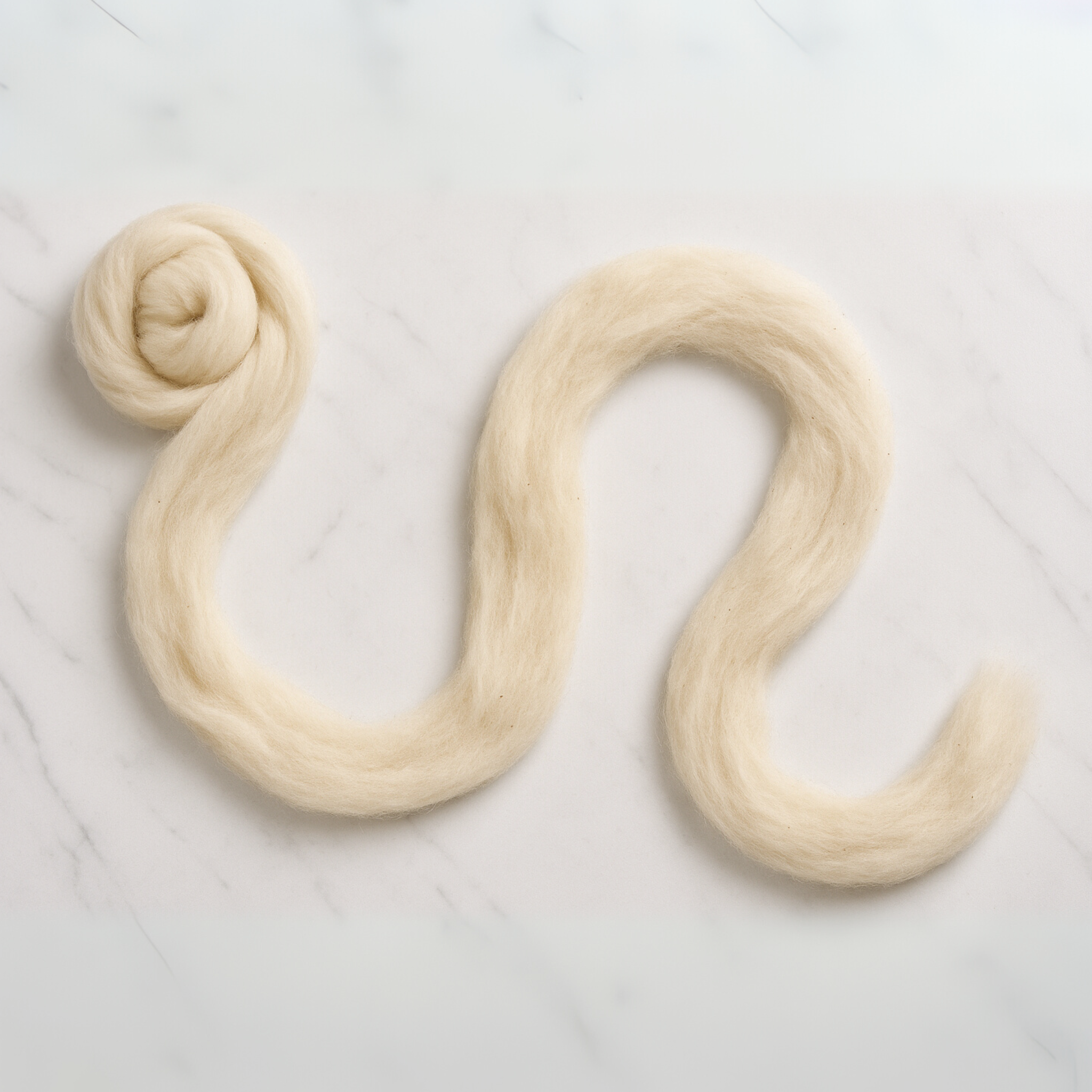 Unraveled strand of natural undyed 19-micron carded Merino wool sliver laid in an S-shape on marble, highlighting the lofty carded texture for spinning and felting.