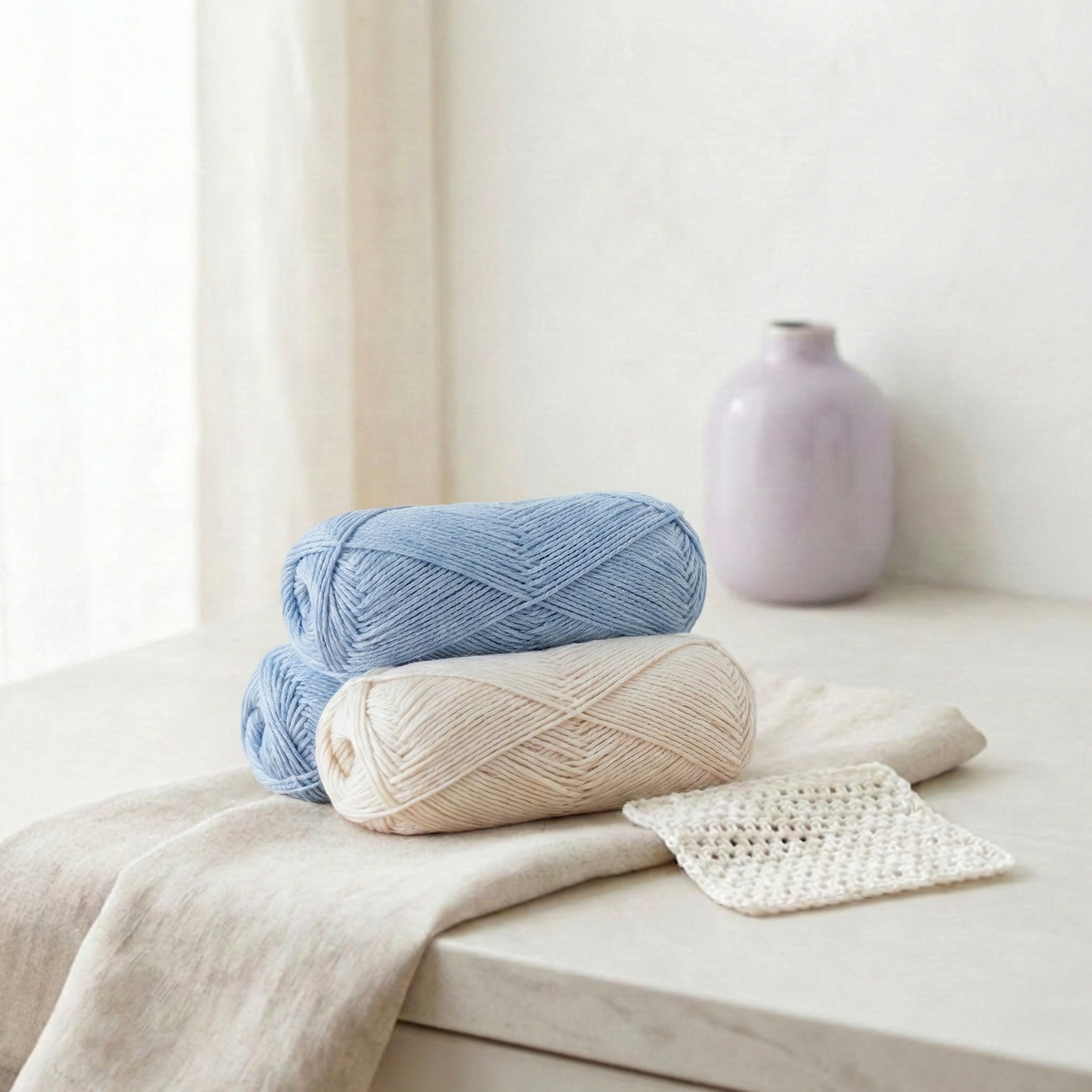 Brown Sheep Lamb’s Pride Worsted yarn in natural cream with knit swatch on a light stone table in bright window light.