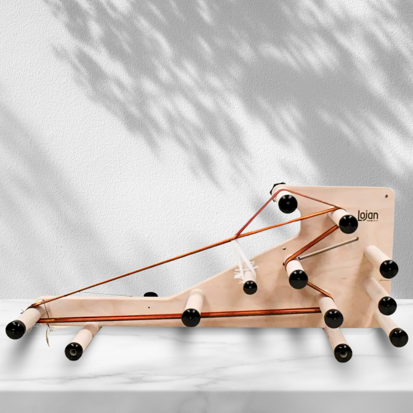 Lojan Inkle Loom by Revolution Fibers set up for tablet weaving, displayed on a marble surface with natural light and shadows, highlighting adjustable pegs and smooth beech wood construction for precise band weaving projects.