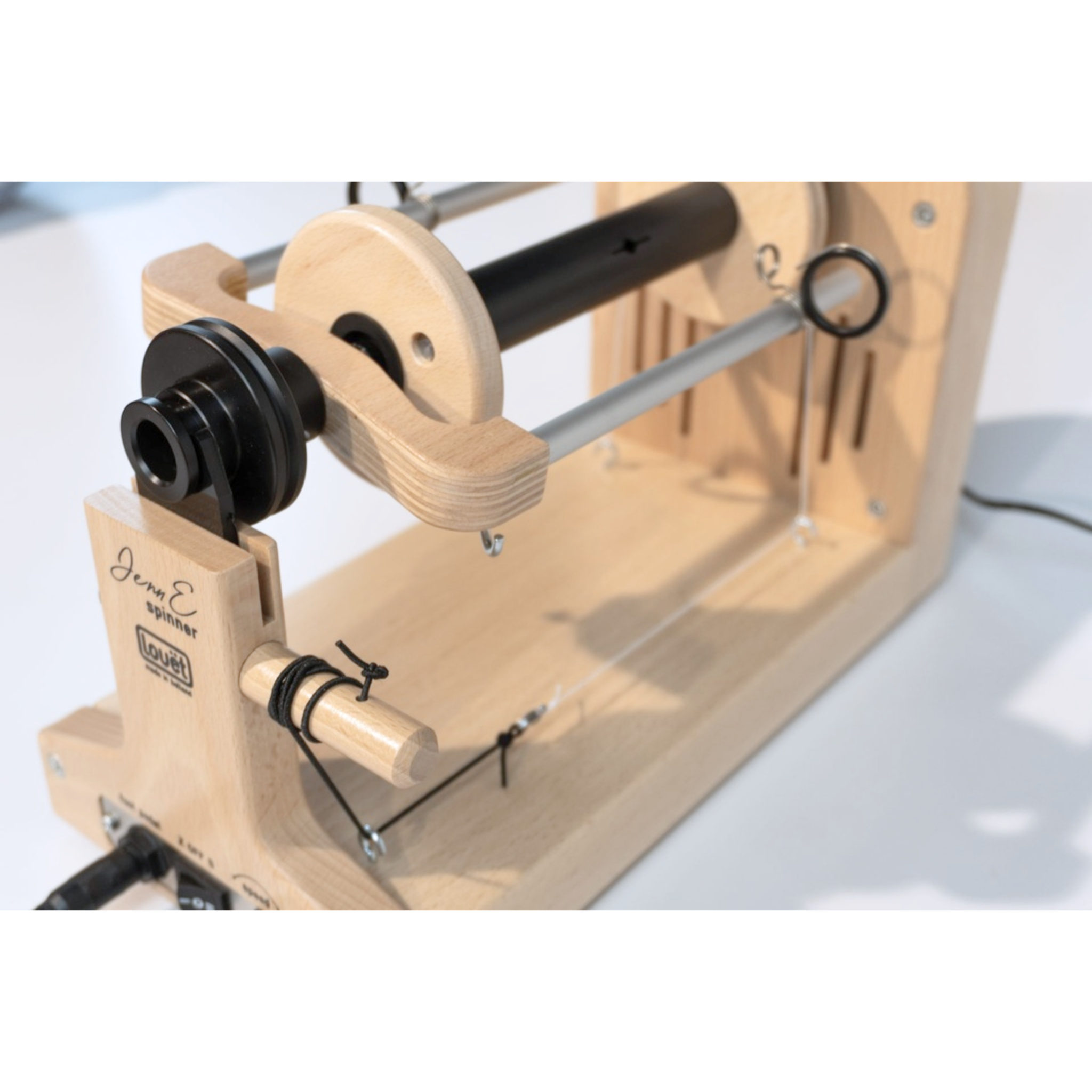 Side-angle view of the Louet Jenn E electric spinning wheel plugged in, highlighting its slim profile and drive system.