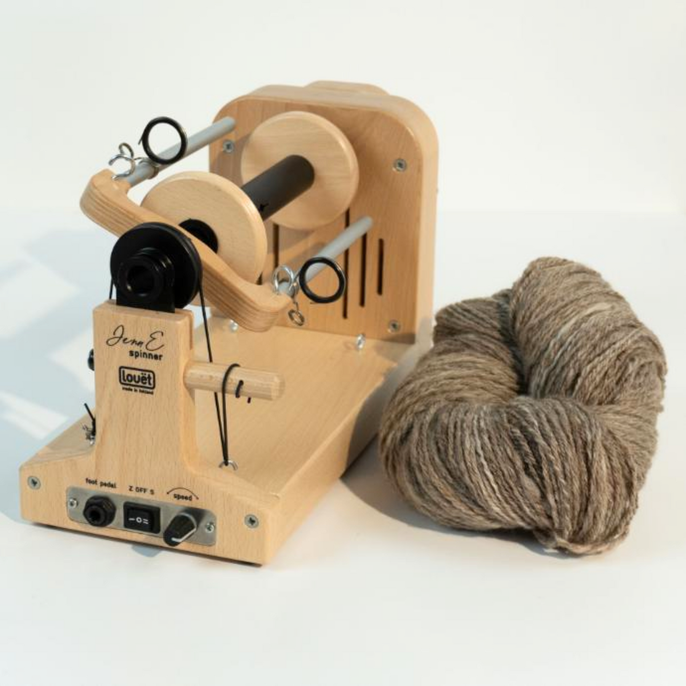 Louet Jenn E electric spinning wheel beside a skein of hand-spun grey wool, illustrating the wheel’s production capacity.