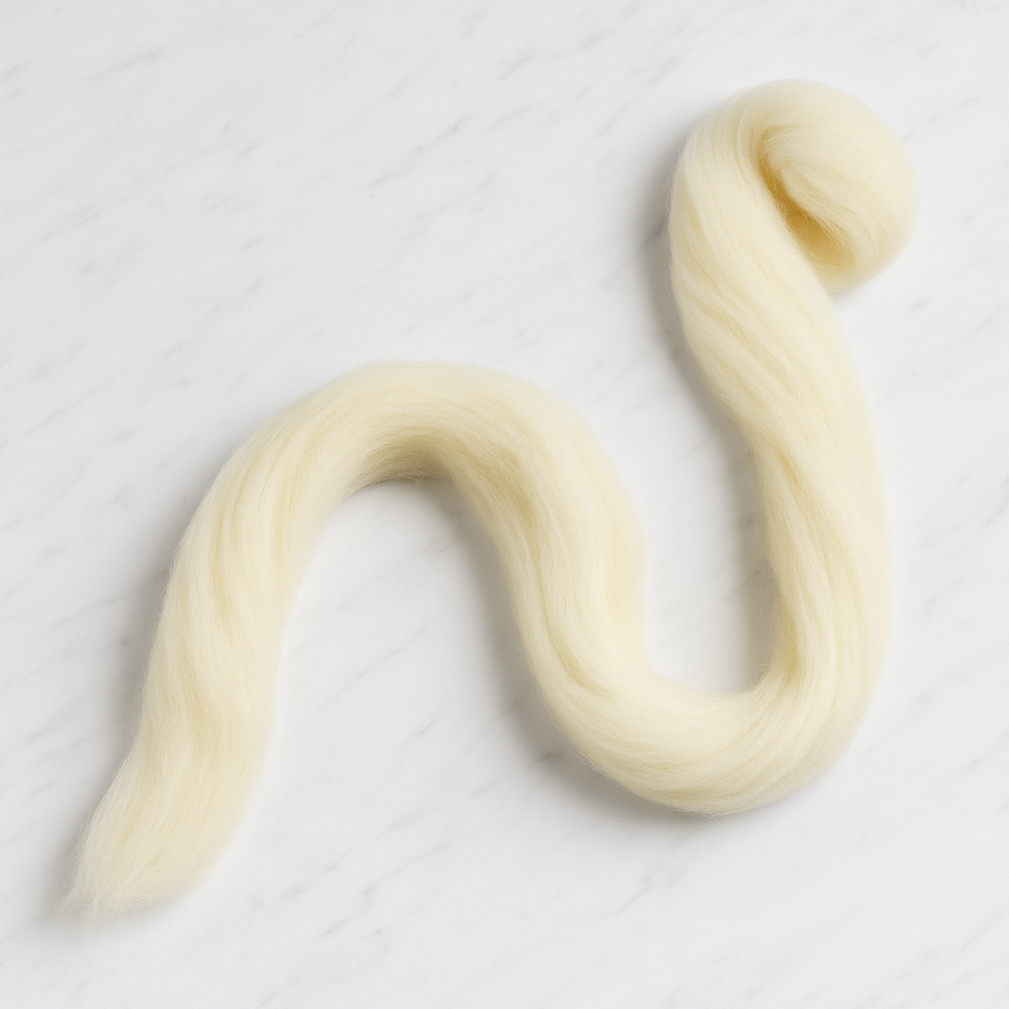 Revolution Fibers Targhee wool combed top partially unraveled strand on white marble background, continuous cream fiber ideal for spinners and dyers.