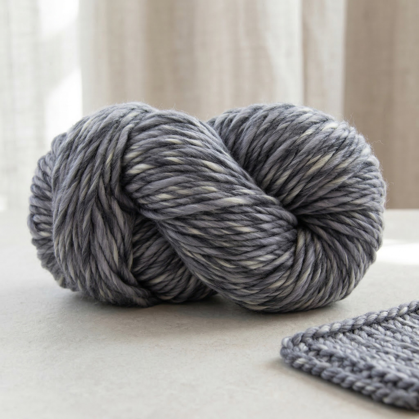 Tempest Gray super bulky multicolor merino wool yarn skein styled on a neutral surface with a knitted swatch in a calm editorial scene.