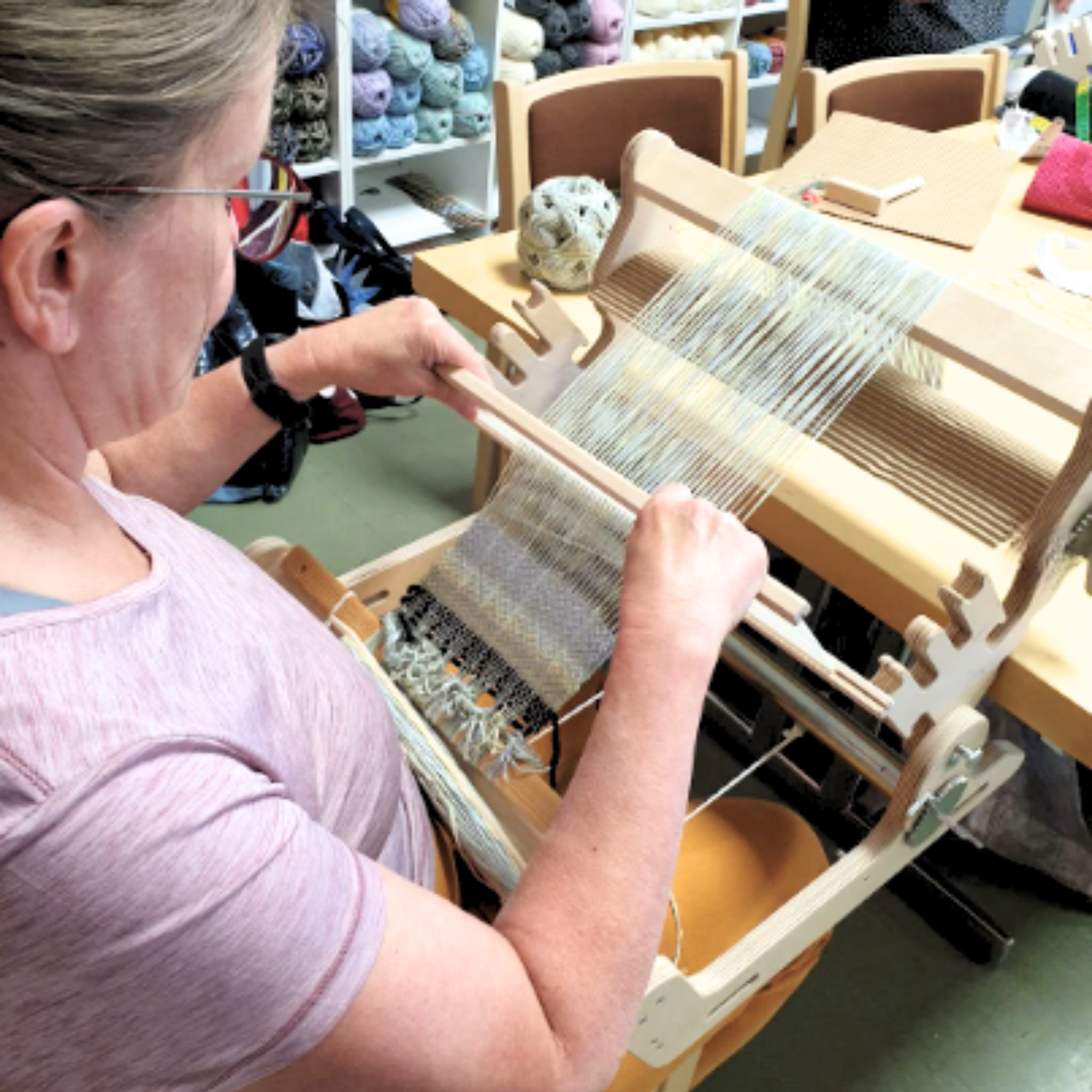 A weaver working on the Glimakra Siru Rigid Heddle Loom in a workshop setting, demonstrating its ergonomic design and smooth weaving process.