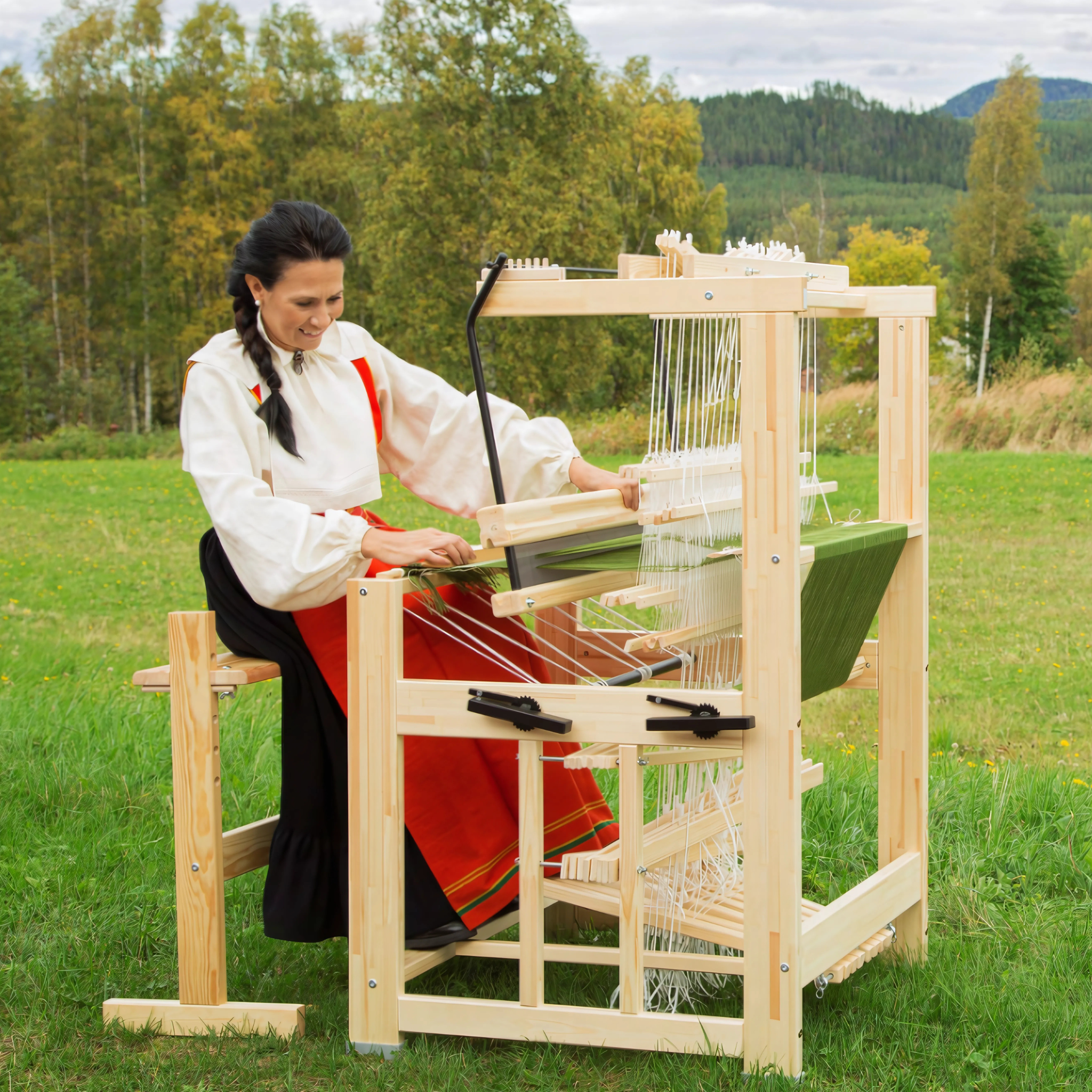 A woman in traditional Scandinavian attire weaving on the Glimakra Julia Floor Loom outdoors. The compact and sturdy loom is ideal for creating high-quality textiles, offering both counterbalance and countermarch configurations for precise weaving control.