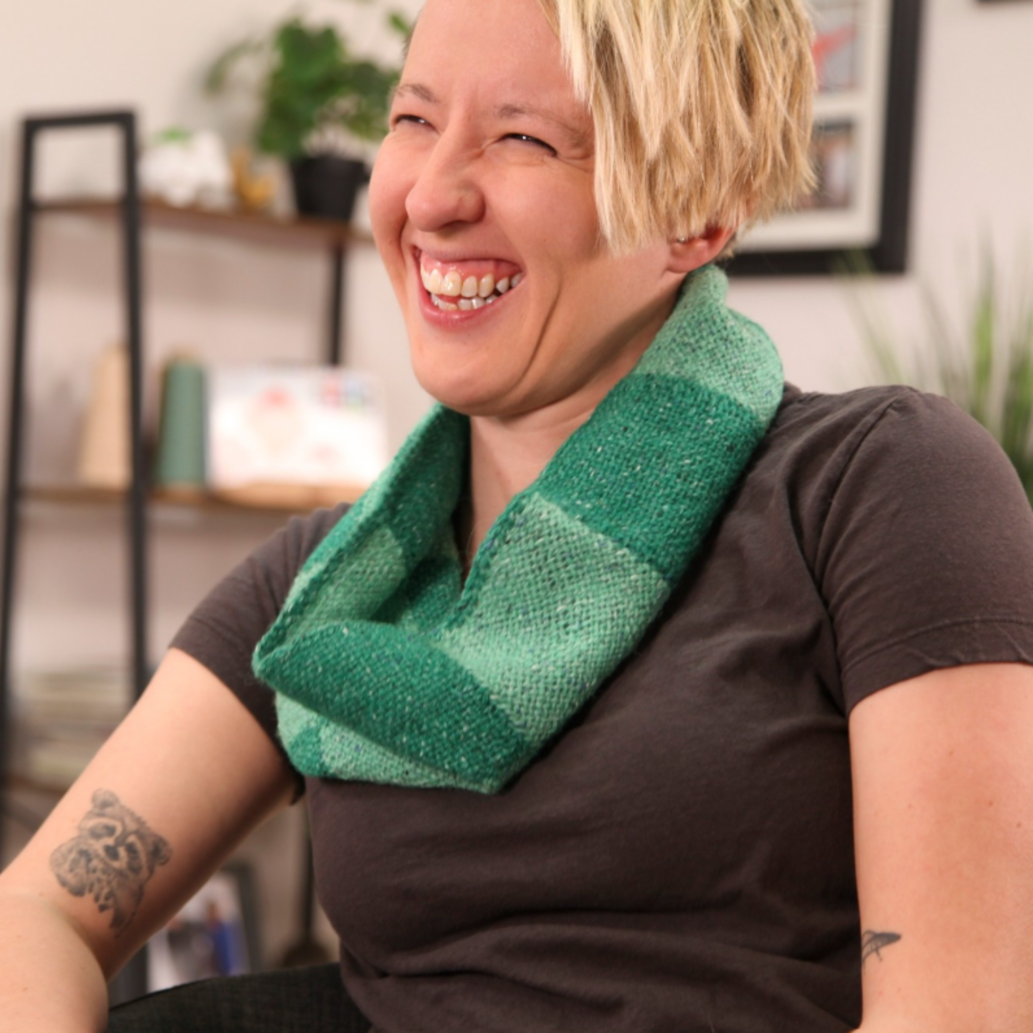 A smiling woman wearing a handwoven green cowl made from woven squares created on the Schacht Zoom Loom. The soft and textured fabric highlights the versatility of the portable pin loom.